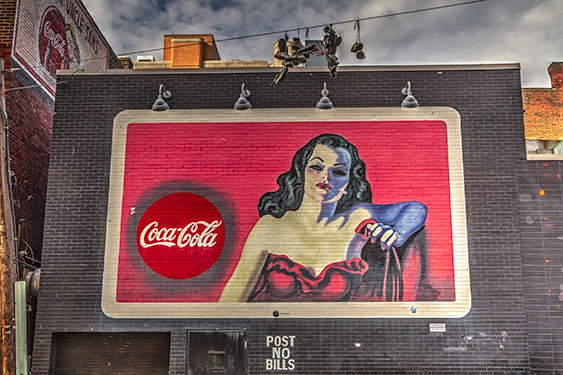 A billboard in the Oakland area of Pittsburgh displaying an old coca cola sing on the side of a building.