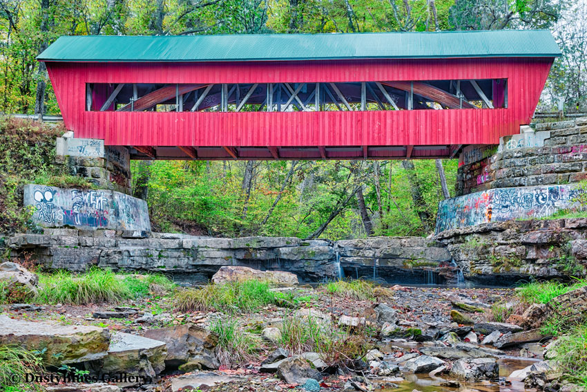 A classic lonely covered bridge spans a deep gorge. Prolific descriptive  graffiti indicates a gathering place for local youths...